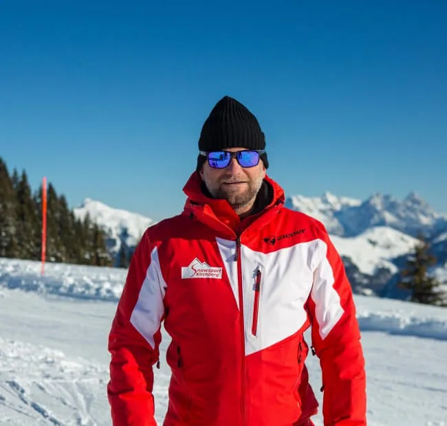 Mann in roter Skijacke mit Sonnenbrille im Schnee