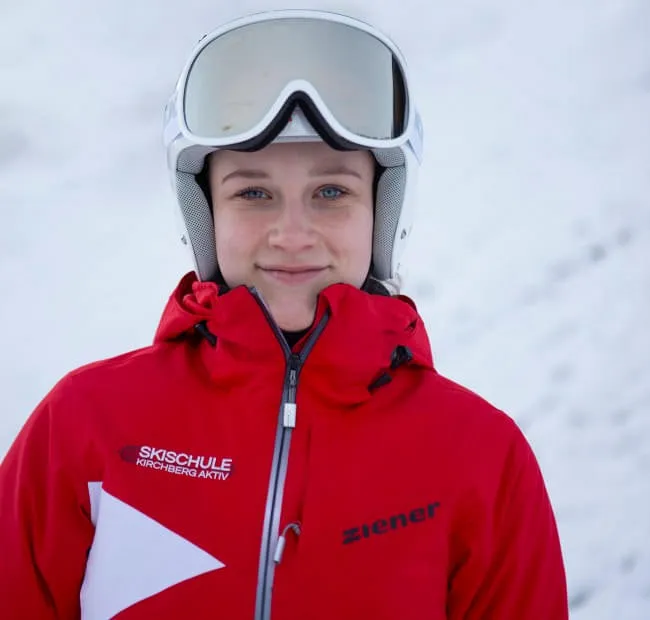 Lächelnde Person in roter Skijacke mit Skihelm