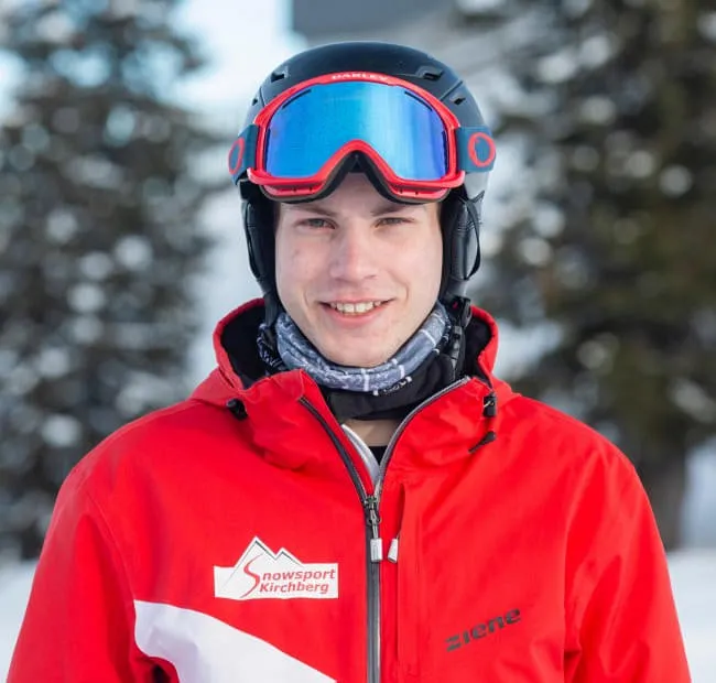 Mann mit Skiausrüstung in roter Jacke, Schnee im Hintergrund